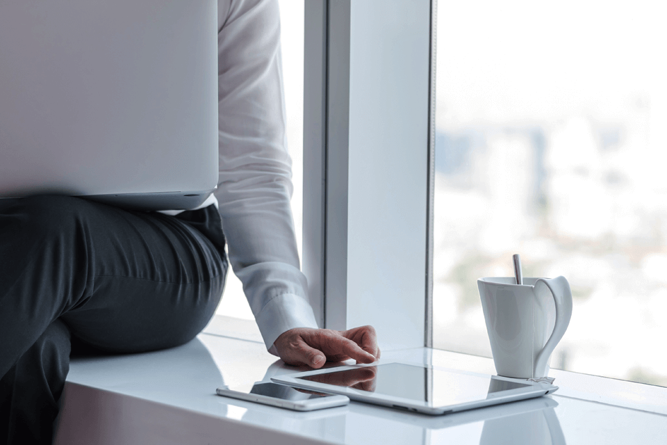 Businessman on the window side looking at his laptop and tablet with a cup of coffee. Businessman on the window side looking at his laptop and tablet with a cup of coffee.